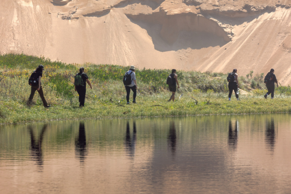 Image of Fellows walking alongside the river, with their reflections in the water